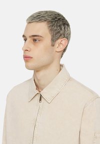 Giacca beige chiaro con colletto a punta, chiusura frontale con zip e maniche lunghe, caratterizzata da una texture sottile e un design pulito.