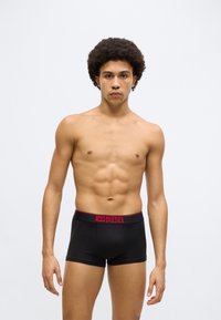 Boxeri negri cu talie elastică roșie, pe care este inscripționat numele mărcii "DIESEL" cu litere îndrăznețe, expuși pe un fundal neutru.