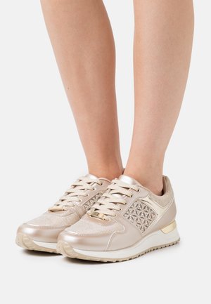 Sneakers beige metallizzate con tessuto strutturato, design geometrico dettagliato, chiusura con lacci e colletto imbottito. Suola in gomma con lieve rialzo.