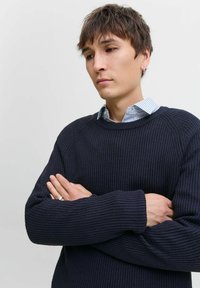 Navy ribbed knit sweater with long sleeves, round neckline, and textured fabric. Layered over a light blue and white striped shirt.