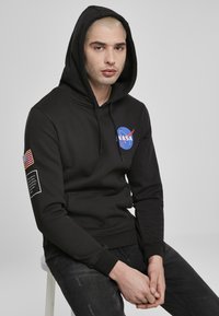 Fekete kapucnis pulóver pamut keverékből, kék és piros NASA logóval a mellkason, amerikai zászló folttal az ujjon, és kenguru zsebbel.