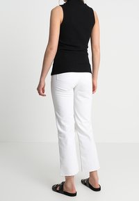 Černý žebrovaný tílko bez rukávů, spárováno s bílými zkrácenými džíny s roztrhaným lemem a černými sandály, pohled zezadu.