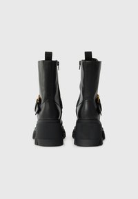 Black leather ankle boots with a chunky platform sole, side zippers, and pull tabs. Features a small gold accent on the side.
