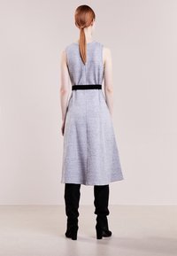 Robe sans manches grise avec un corsage ajusté et une jupe évasée, soulignée par une ceinture noire. Caractérisée par une texture lisse et un ourlet arrivant au genou.