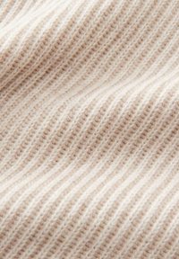 Cremfarbener gerippter Wollstoff mit weicher Textur und diagonalen Falten, die Strickdetails und das Fasermuster zur Geltung bringen.