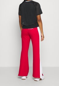 Black mesh cropped t-shirt with short sleeves paired with flared red pants featuring white side stripes. Visible logo on the waistband.