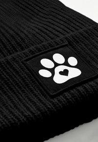 Black knitted beanie featuring a square patch with a white paw print and heart design, providing a textured appearance.