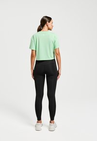 Haut de sport cropped vert menthe à manches courtes associé à un legging noir taille haute et des baskets blanches. Design simple, texture lisse.