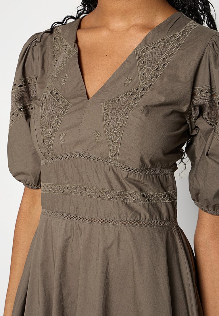 Olivgrünes Kleid mit V-Ausschnitt, kurzen Puffärmeln, filigraner Stickerei und Spitzenbesatz an der Taille und dem Saum. Weicher, strukturiertes Material.