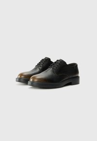 Scarpe eleganti in pelle nera e marrone con una texture liscia, punta tonda e design con lacci. Presentano una suola in gomma bassa e resistente.