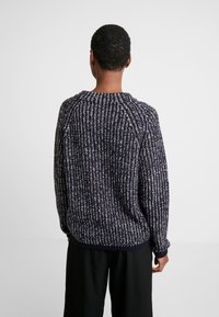 Mörkblå stickad tröja med vita prickar, med ribbad textur, rund halsringning och nedhasade axlar, kompletterad med en avslappnad passform.