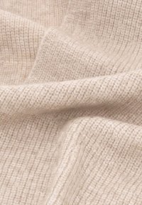 Tessuto a maglia di un beige chiaro con una texture a coste. Il materiale appare morbido e leggermente elastico, mostrando sottili variazioni di colore.