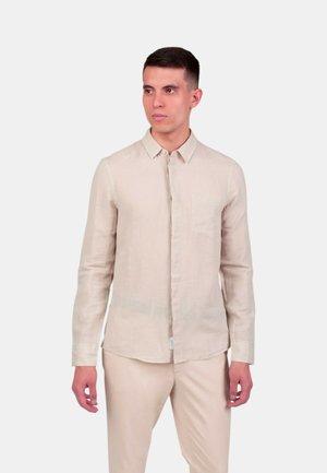 Camicia di lino beige chiaro con design a bottoni, maniche lunghe e taschino sul petto, abbinata a pantaloni di colore chiaro coordinati.