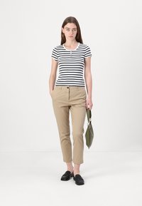 Stripete kortermet polo skjorte i hvit og marineblå, kombinert med beige chinos. Modellen holder en grønn veske og har på seg svarte loafers. Enkelt design.