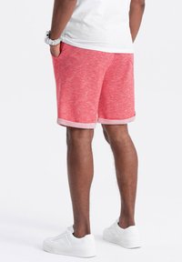 Shorts rouge chinés avec une finition texturée, présentant des ourlets roulés et des poches latérales, associés à des baskets blanches.
