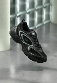 Μαύρο αθλητικό παπούτσι με πλέγμα και καουτσούκ σόλα. Διακοσμημένο με ασημένιες λεπτομέρειες και σχεδιασμό με κορδόνια. Ελαφρύ και διαπνέον.