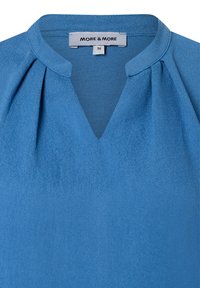 Blaue Bluse mit V-Ausschnitt, plissiertem Detail und glatter Textur. Das Etikett zeigt die Marke "MORE & MORE" und die Größe 36.