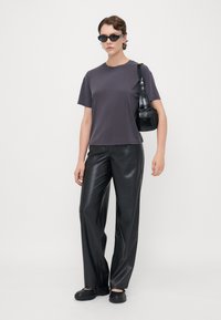T-shirt gris à manches courtes, associé à un pantalon large en simili cuir noir. Les accessoires comprennent des lunettes de soleil noires et un petit sac à main.