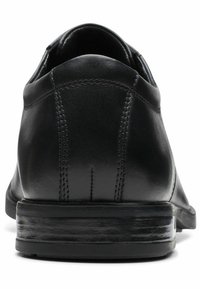 Scarpa in pelle nera con finitura liscia, tallone arrotondato e dettagli di cucitura sottili lungo le cuciture, dotata di una suola bassa e testurizzata.