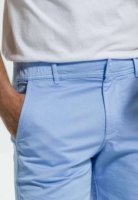 Shorts bleu clair en coton lisse, dotés d'une taille élastique, de poches latérales et de détails de couture subtils.
