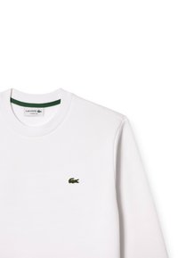 Felpa bianca Lacoste con colletto tondo, dettaglio verde al colletto e piccolo logo coccodrillo verde sul petto. Tessuto morbido.