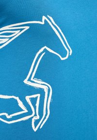 Blue cotton T-shirt featuring a white abstract design of a leaping horse on the front. The texture is soft and the fabric appears smooth.