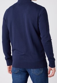 Marinblå tröja med hög krage, långa ärmar och ribbad nederkant. Tillverkad av mjukt material med slät textur, figurnära design.