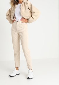 Beige kordjacka med kapuschong, i cropped modell, kombinerad med högmidjade beige kordbyxor och vita sneakers. Enkelt design och textur.