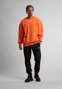 Oransje bomullssweatshirt med ribbestrikkede mansjetter, hvit "STARTER" logo. Sammen med svarte joggebukser med logo og snøring. Svarte sneakers.