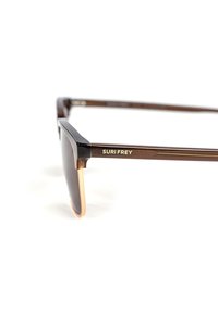 Brune solbriller med en blank, vinkelret ramme. Mørke linser, orange kant og guldfarvet "SURI FREY" branding på stangen.