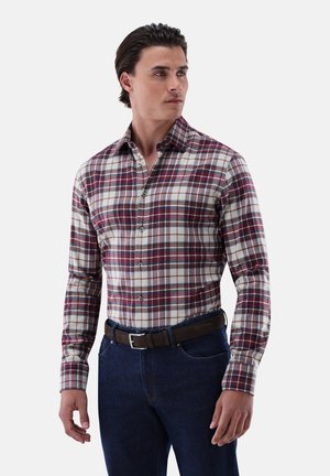 Langärmeliges, knöpfbares Hemd aus Baumwolle mit einem rot, marineblau und cremefarbenen Karomuster. Kombiniert mit dunkelblauen Jeans und einem braunen Ledergürtel.