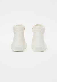 Bottines blanches jusqu'à la cheville en matériau synthétique lisse, avec un détail de fermeture éclair, un col rembourré et une semelle en caoutchouc texturée avec logo.