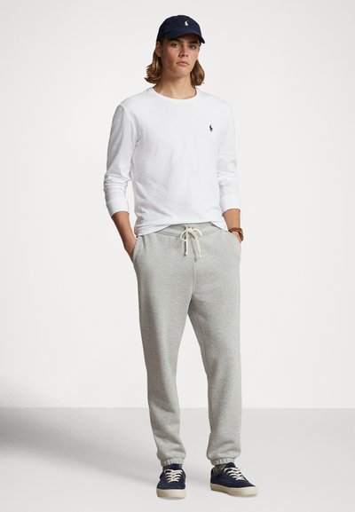 Baltas ilgomis rankovėmis marškinėlis, pilkos sportinės kelnės su raišteliu ir tamsiai mėlyna kepurė. Kasdieniai bateliai tamsiai mėlynos ir kreminės spalvų. Minimalistinis dizainas.