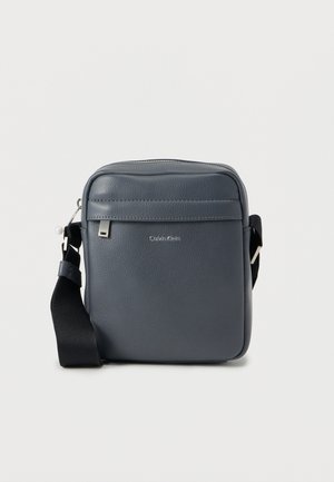 Grå skinn skulderveske med glidelåslukking, flat frontlomme, logodetalj, justerbar svart stropp og glatt tekstur.