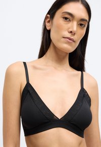 Czarny trójkątny biustonosz typu bralette z cienkimi, regulowanymi ramiączkami i przejrzystymi siateczkowymi elementami wzdłuż dekoltu. Gładka tkanina o minimalistycznym designie.