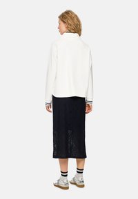 Weißes Sweatshirt mit Kragen und Marineblauem Spitzenrock. Verfügt über gestreifte Bündchen und dekorative Muster. Die Schuhe umfassen gemusterte Sneakers.