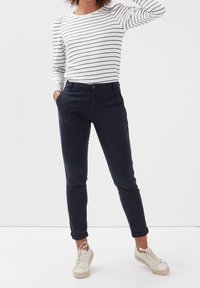 Celana navy biru yang dipotong rapi dengan fit ramping, terbuat dari kain lembut. Dipasangkan dengan kemeja lengan panjang bergaris putih dan sneakers ringan.