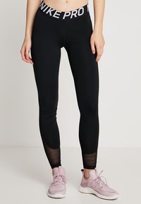 Svarta sport leggings med en bred midjeband där "NIKE PRO" är tryckt i vitt. Texturerade paneler vid vaden ger visuell intress. 
