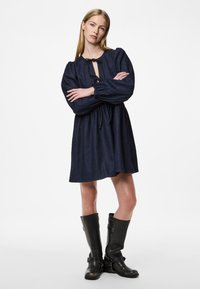 Vestido de ganga azul-marinho com mangas bufantes, decote com laço e bainha rodada, combinado com botas de couro pretas até ao joelho.