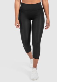 Leggings capri neri con una vita alta, texture liscia e lunghezza fino a metà polpaccio, abbinati a scarpe da ginnastica bianche.