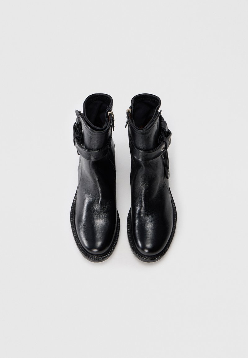 Ein Paar schwarze Lederstiefeletten mit seitlichen Reißverschlüssen und geschnallten Riemen, von oben auf einem weißen Hintergrund gezeigt.