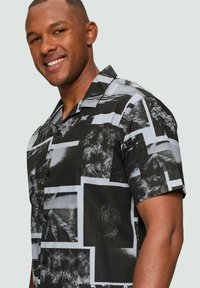 Korte mouwen zwart-witte shirt met een collage van ingelijste patronen, gedrukt op lichtgewicht stof, met een kraag en knoopsluiting.