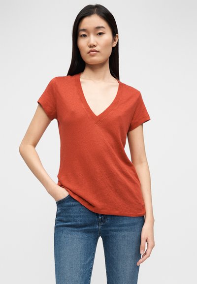 Punane lühikeste varrukatega V-kaelusega T-särk, valmistatud kergest kangast, millel on lõdvestunud lõige ja peen tekstuur, kombineeritud siniste teksapükstega.