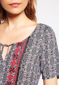 Black and white patterned dress with red accents, featuring a V-neckline and tie closure, short sleeves, and textured fabric.