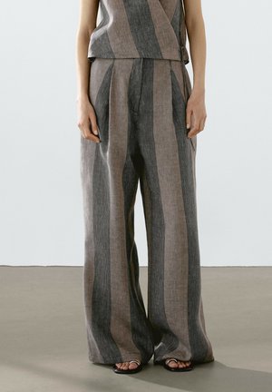 Femme portant un pantalon large et ample à jambes larges avec des rayures verticales grises et beiges, associé à un haut rayé assorti et des sandales noires.