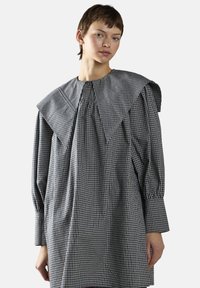 Rutig kjole i sort og hvid med en bred, spids krave, lange ærmer og en flydende silhuet med samlede detaljer.