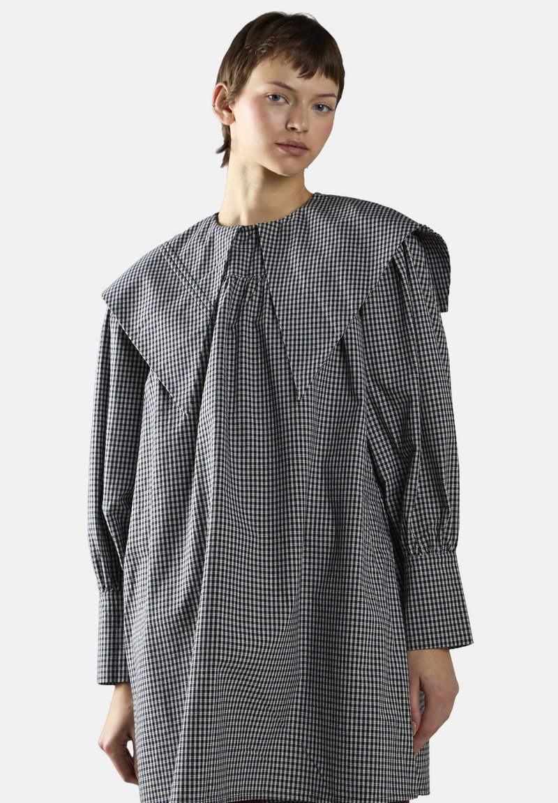 Rutig kjole i sort og hvid med en bred, spids krave, lange ærmer og en flydende silhuet med samlede detaljer.