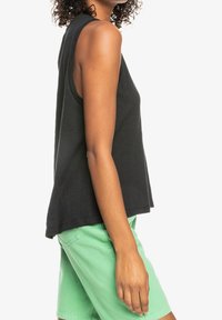 Haut sans manches noir avec une coupe décontractée, fabriqué en tissu léger, présentant un col rond et un ourlet légèrement incurvé. Assorti avec un short vert.