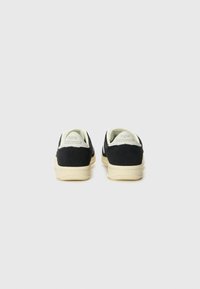 Sorte semskede sneakers med kremfargede såler og detaljer. Har polstret ankelkrage og preget logo på hælen. Glatt tekstur.