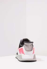 Black and gray sneaker with pink accents, mesh upper, cushioned collar, and textured rubber sole. Sleek design with a modern silhouette.